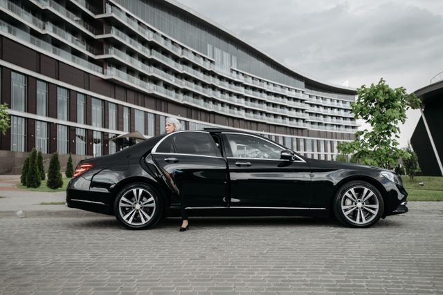 Senior businesswoman exiting a sleek black car in front of a modern building.